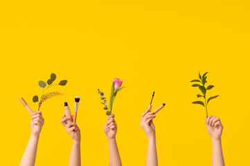 Female hands with tulip, concealer, foundation, brush, mascara and branches on yellow background