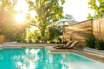 Swimming pool in modern private villa with lounge chairs, palm trees and umbrella
