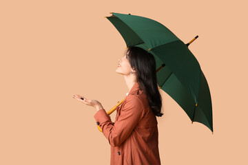 Young woman with opened umbrella on beige background