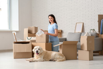 Young happy woman and cute Labrador dog with boxes on moving day at home