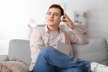 Fototapeta premium Young man listening to audiobook and using tablet on sofa in living room