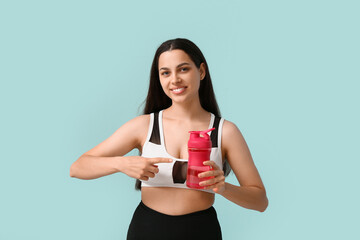 Beautiful young happy woman pointing at sports bottle of water on blue background