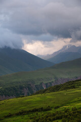 Majestic view of beautiful green valley with colorful grass against the backdrop of picturesque high mountains in cloudy weather