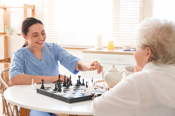 Physical therapist with senior woman playing chess at table in kitchen