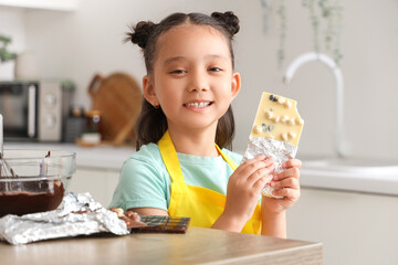 Cute little Asian girl with white chocolate bar in kitchen