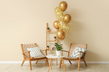 Beautiful golden air balloons with chairs and coffee table near beige wall at home