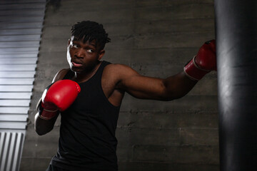 Powerful African American boxer wearing red gloves prepares to hit punching bag in gym showing his...