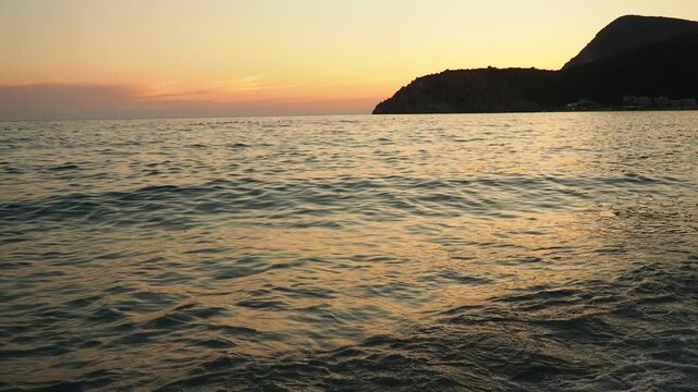 Waves gently lap at shore during stunning sunset over ocean. Golden sunlight reflects off waves as they roll onto shore, creating tranquil atmosphere at sunset by sea. Montenegro summer Canj