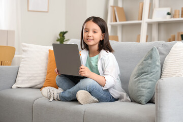 Fototapeta premium Little Asian girl using laptop on sofa at home