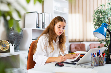 Young clerical worker sitting at desk in office and using laptop for work.