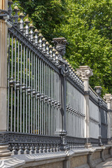 A metal black old wrought fence on the green trees background. Vertical photo