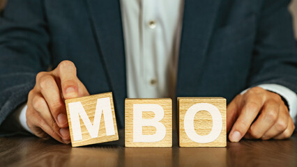 There is wood cube with the word MBO. It is an abbreviation for Management by Objectives as...