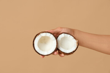Female hand with halves of fresh coconut on brown background
