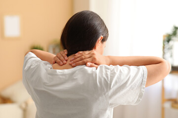Young woman suffering from neck pain at home, back view