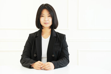 Young asian woman with black hair against white wall, front view.