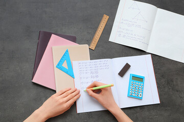 Woman writing math formulas in copybook on dark background
