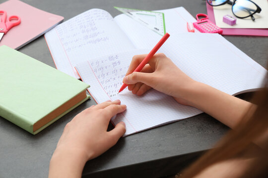 Woman writing math formulas in copybook at dark table