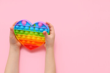Child's hands with pop it fidget toy heart-shaped on pink background, closeup