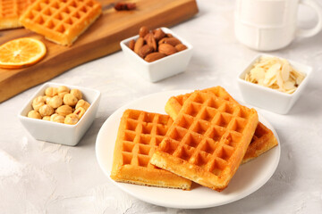 Plate with tasty Belgian waffles and bowls of different nuts on grey background