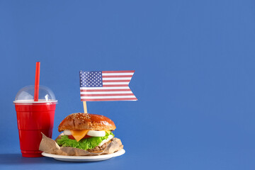 Tasty burger with flag of USA and cola on blue background. American Independence Day celebration