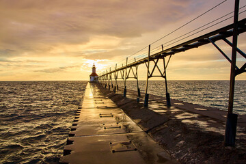 Obraz premium Lighthouse at Sunset with Pier Reflection Low Eye-Level Perspective