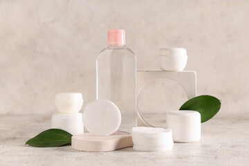 Bottle of micellar water, green leaves, plaster stands and cotton pads on grunge background