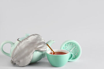 Sleep mask, alarm clock, cup of tea and teapot on grey background