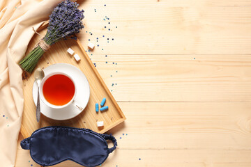 Cup of tea with lavender flowers, sleep mask and pills on wooden background