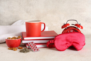 Cup of tea with pretzels, sleep mask, books, pills and alarm clock on white background