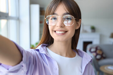 Young woman in eyeglasses taking selfie at home, closeup