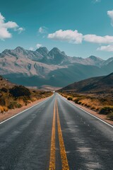 Fototapeta premium A scenic road stretches toward majestic mountains under a clear blue sky.