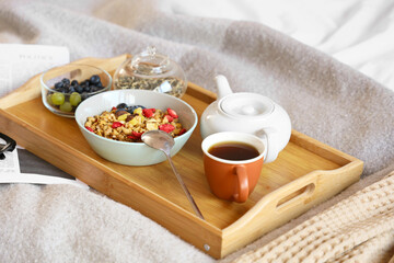 Breakfast in bed with cereals, tea and fruits on tray in bedroom. Closeup