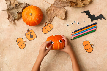 Child with supplies making Halloween decorations on grunge beige background