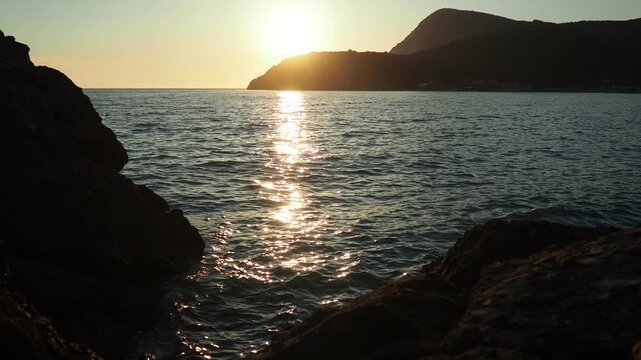 Waves gently lap at shore during stunning sunset over ocean. Golden sunlight reflects off waves as they roll onto shore, creating tranquil atmosphere at sunset by sea. Montenegro summer Canj