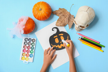 Child with supplies and glue making Halloween decorations on blue background