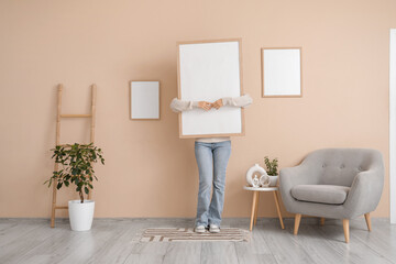 Young woman with blank frame in living room