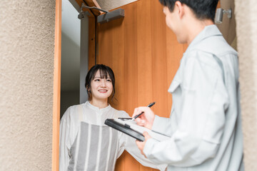 訪問営業・セールスに来た作業着姿の男性を玄関で話を聞く笑顔の主婦
