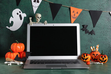 Modern laptop and decor for Halloween celebration on green background