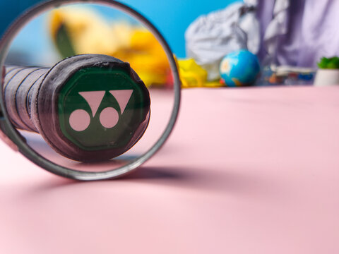 Yonex racket logo closeup with magnifying glass on a pink background