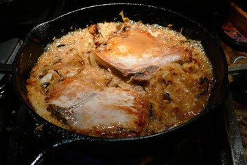 Pork chops sizzling with sauerkraut and onions in cast iron pan