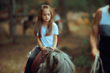 Little Girl Riding a Pony Supervised by an Instructor. Adult supervising a child playing with domesticated horse
