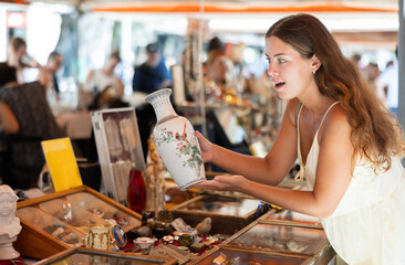 Smiling female tourist looking at various vintage items at street flea market
