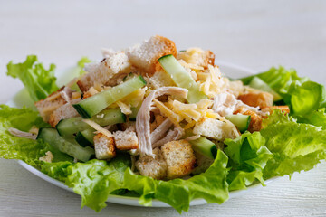 Crunchy salad with chicken, cheese, bread chips and cucumber with lettuce and garlic on a white plate. Healthy eating, close up