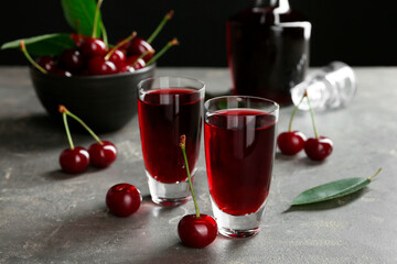 Delicious cherry liqueur in shot glasses and fresh berries on grey table
