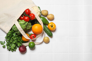Vegan food delivery. Bag with different fresh vegetables and fruits on white tiled table, flat lay. Space for text