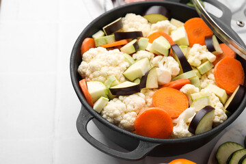Cooking stew. Cut raw vegetables in pot on white tiled table, closeup