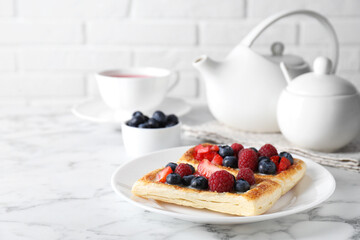 Tasty puff pastries with berries and tea on white marble table, space for text