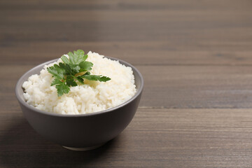 Bowl of delicious boiled rice with parsley on wooden table. Space for text