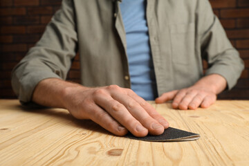 Man polishing wooden plank with sandpaper at table, closeup