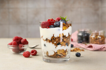 Tasty yogurt with fresh berries, granola and mint in glass on gray textured table